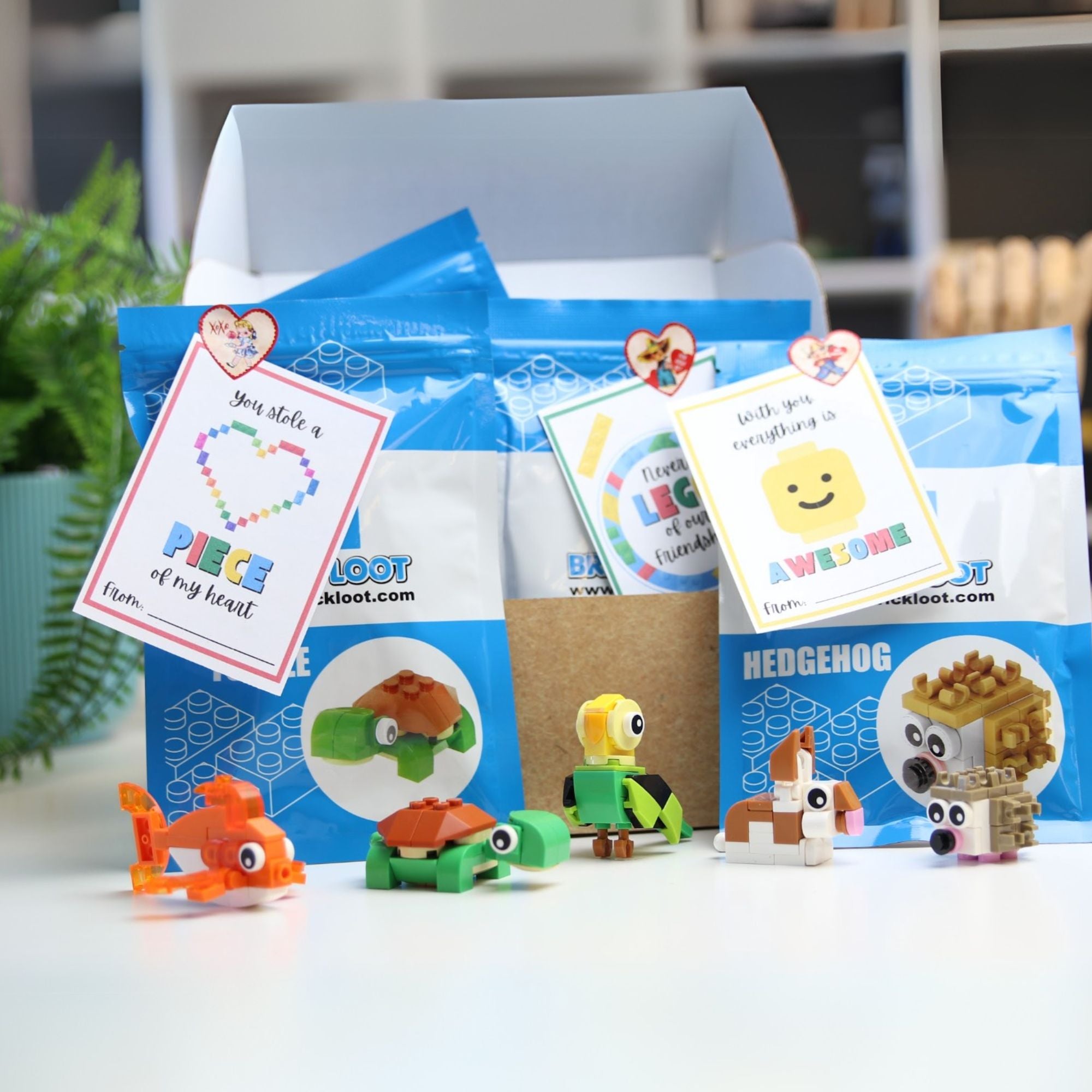 A collection of colorful mini LEGO-compatible build packs designed in animal shapes such as fish, turtle, rabbit, and hedgehog, packaged in a blue box with Valentine's Day themed labels.